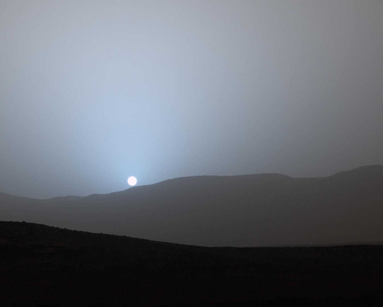 A blue-tinted sunset over the hills of Gale Crater on Mars, photographed by NASA's Curiosity rover.